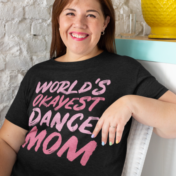 Mamă purtând tricou negru „World’s Okayest Dance Mom” cu mesaj roz, design amuzant pentru mame de balerine.